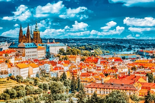 The Prague skyline. It is a blue sky day, the rooftops are orange, the cathedral is in plain sight.